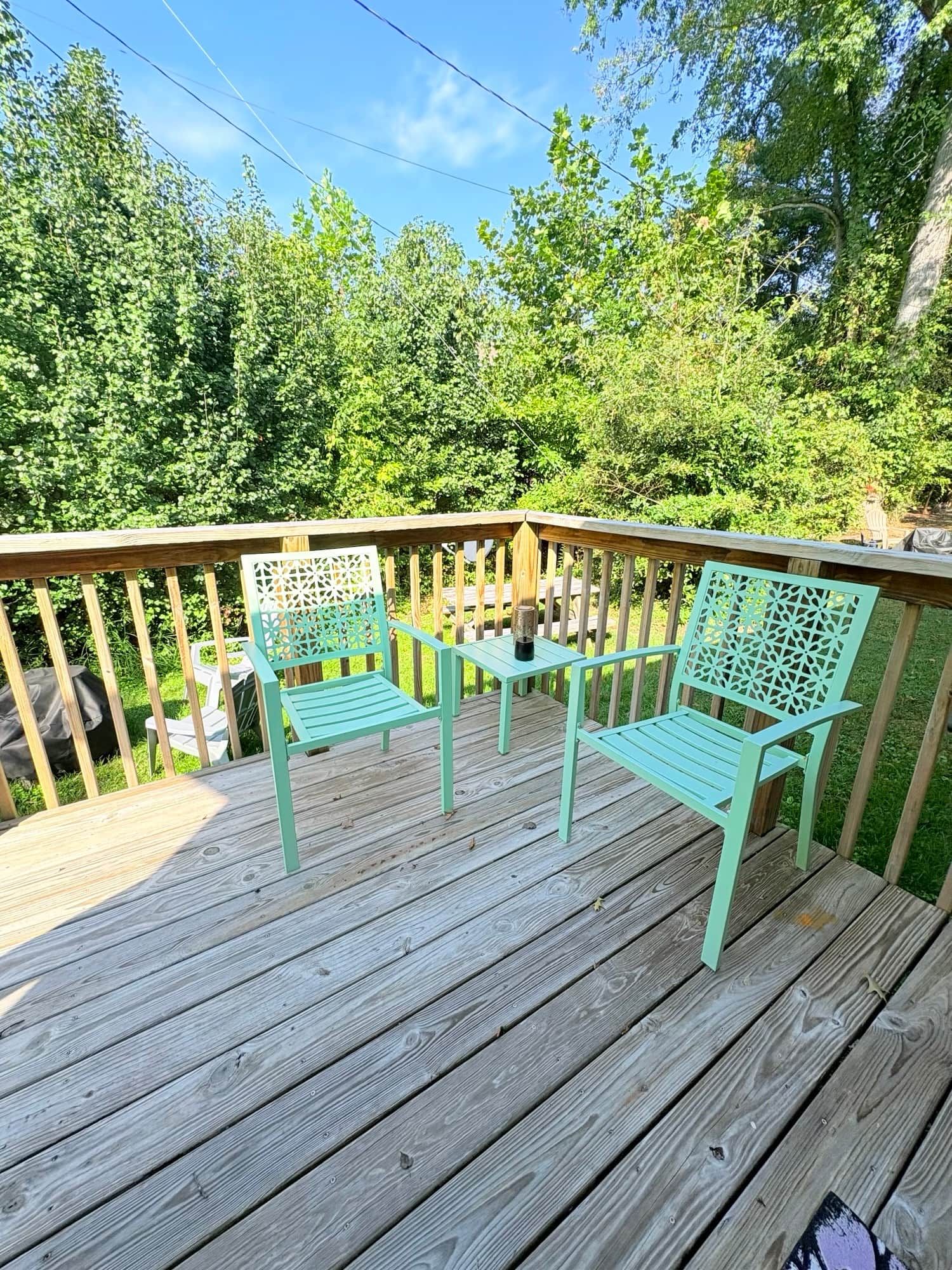 A wooden deck with two chairs and a small table, surrounded by a railing and greenery.