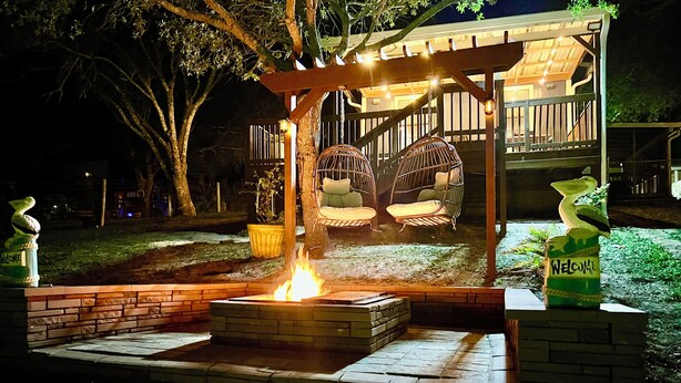 Ein Feuerkorb, umgeben von Ziegelbänken, eine Pergola mit Hängesesseln und ein freundliches Schild.