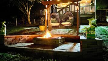 A fire pit surrounded by brick seating, a pergola with hanging chairs, and a welcoming sign.