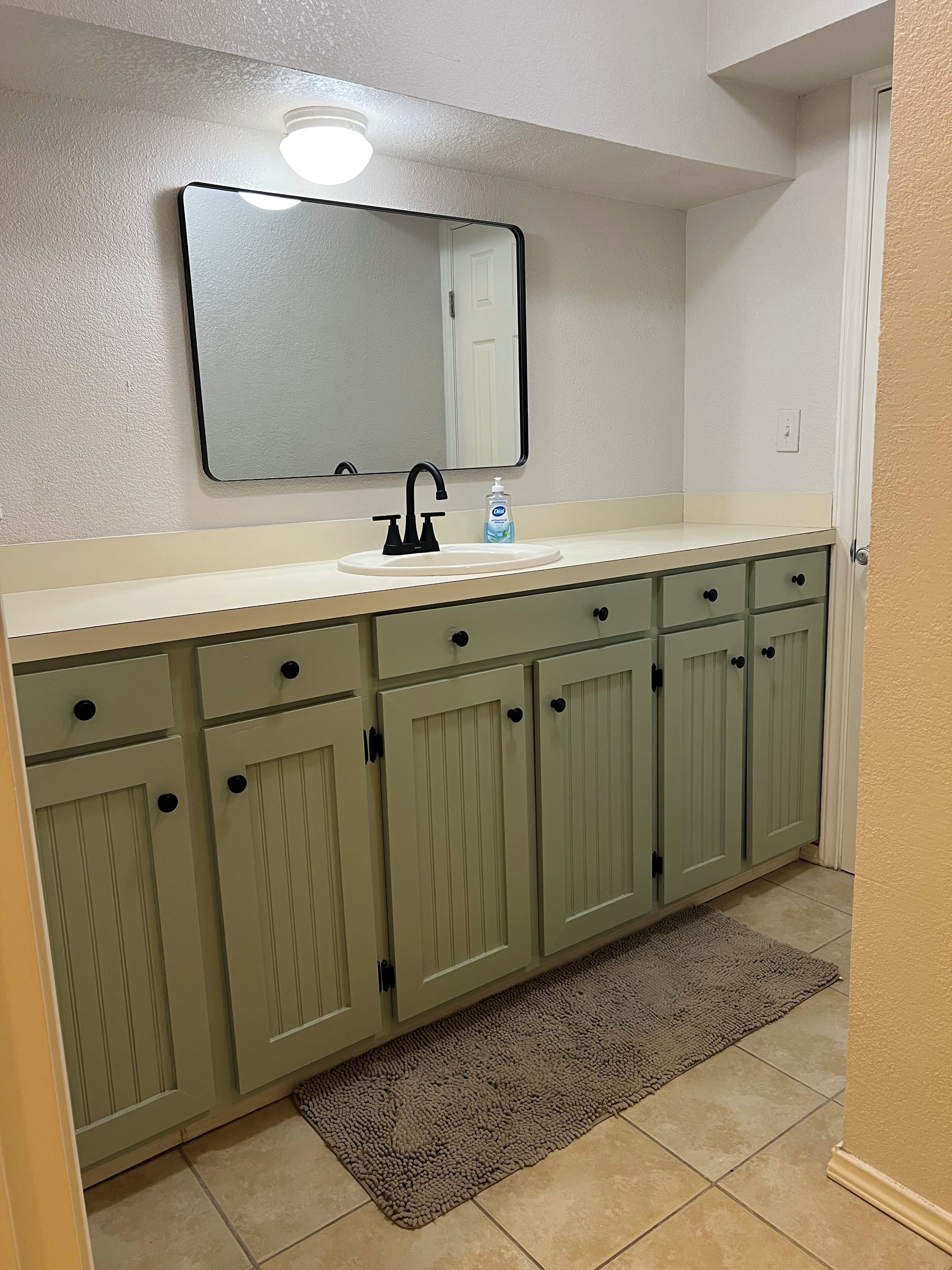 A bathroom with a white sink, a mirror above it, and green cabinets below.