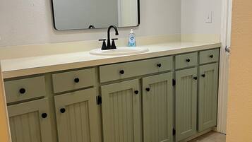 A bathroom with a white sink, a mirror above it, and green cabinets below.