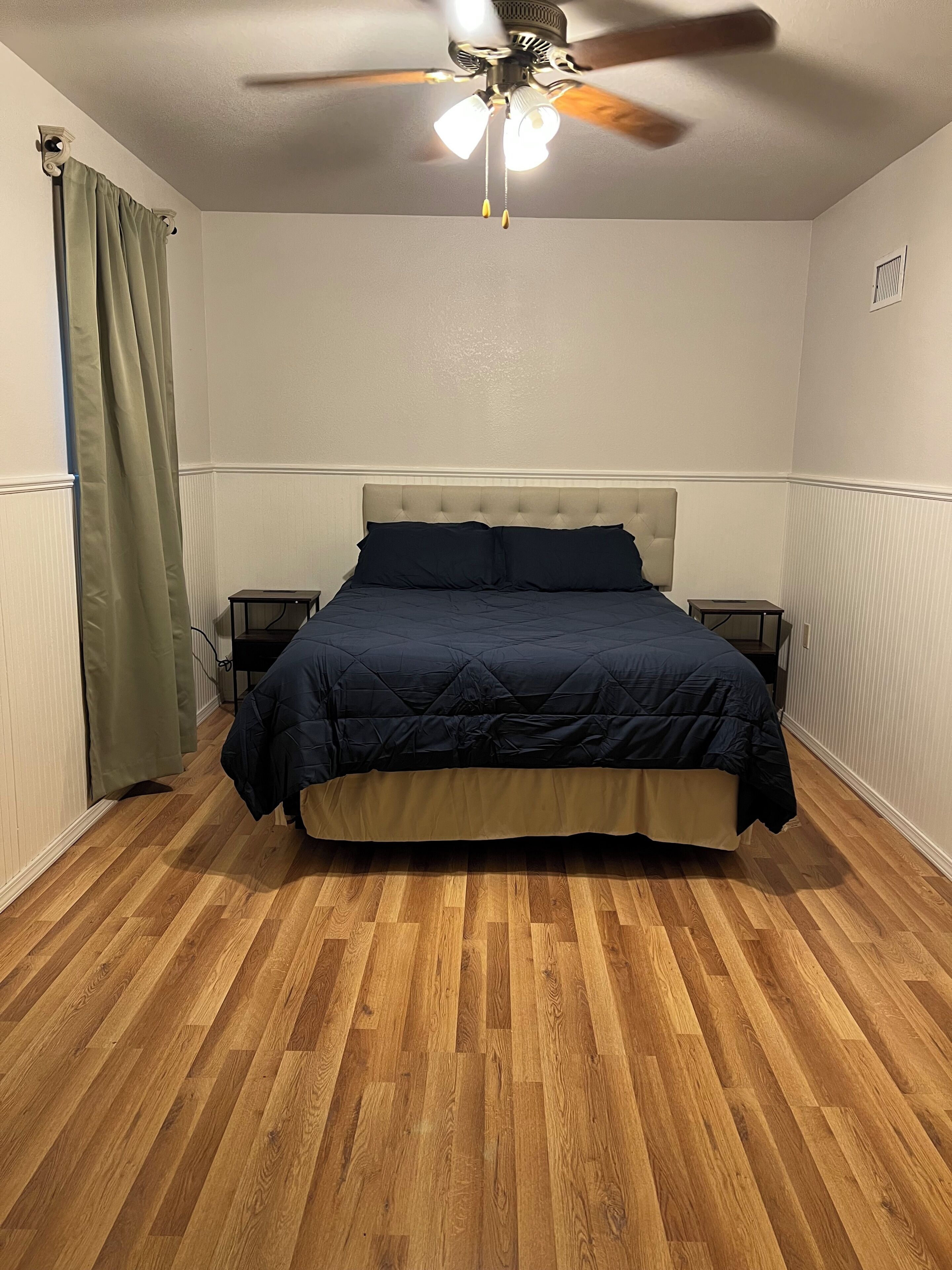 A bedroom with a bed, a ceiling fan, and a nightstand.