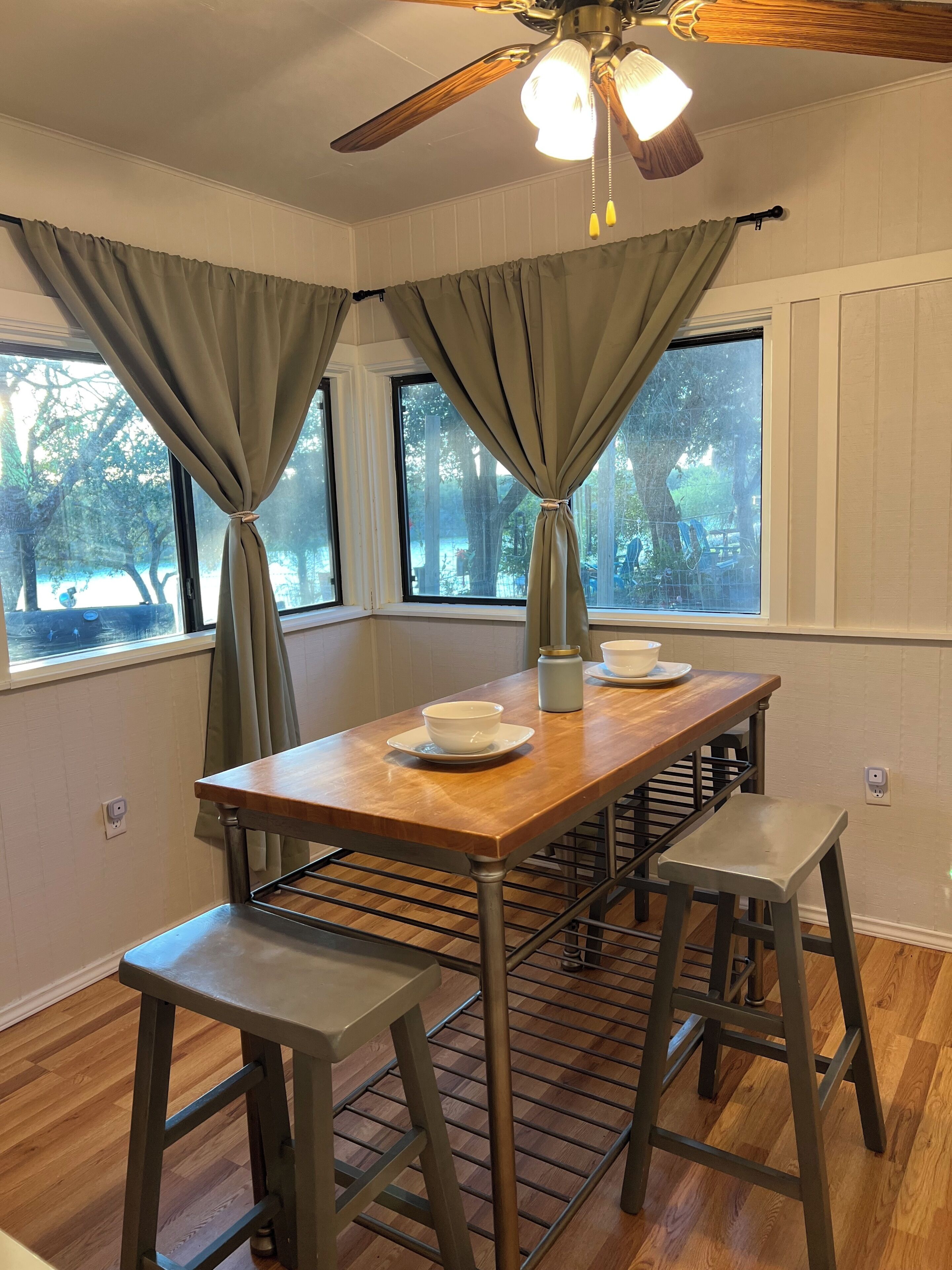 A dining area with a wooden table, two stools, and a ceiling fan.