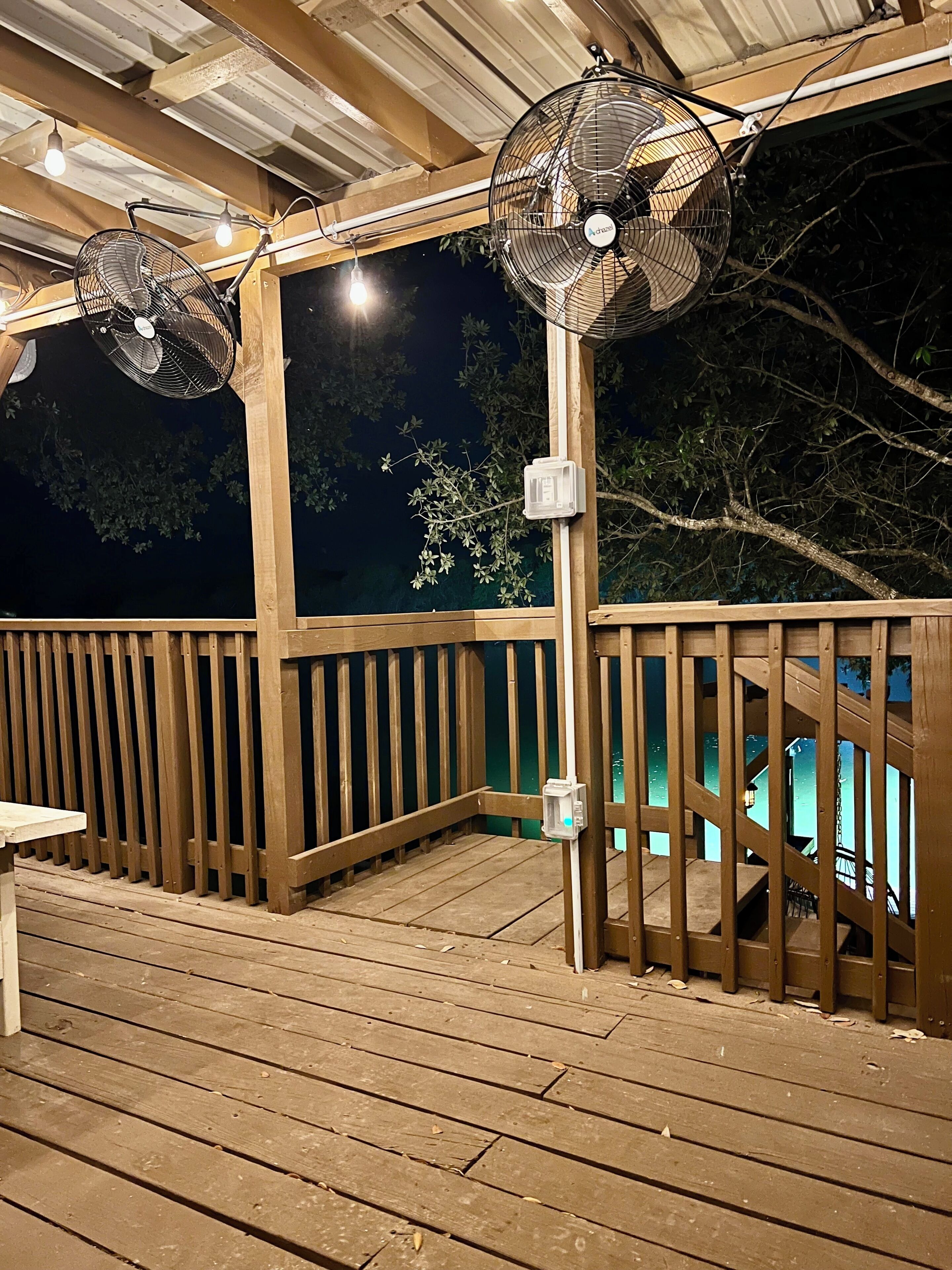 Eine Holzterrasse mit zwei Ventilatoren, einem Geländer und Blick auf den Nachthimmel.