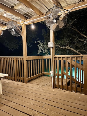 A wooden deck with two fans, a railing, and a view of the night sky.