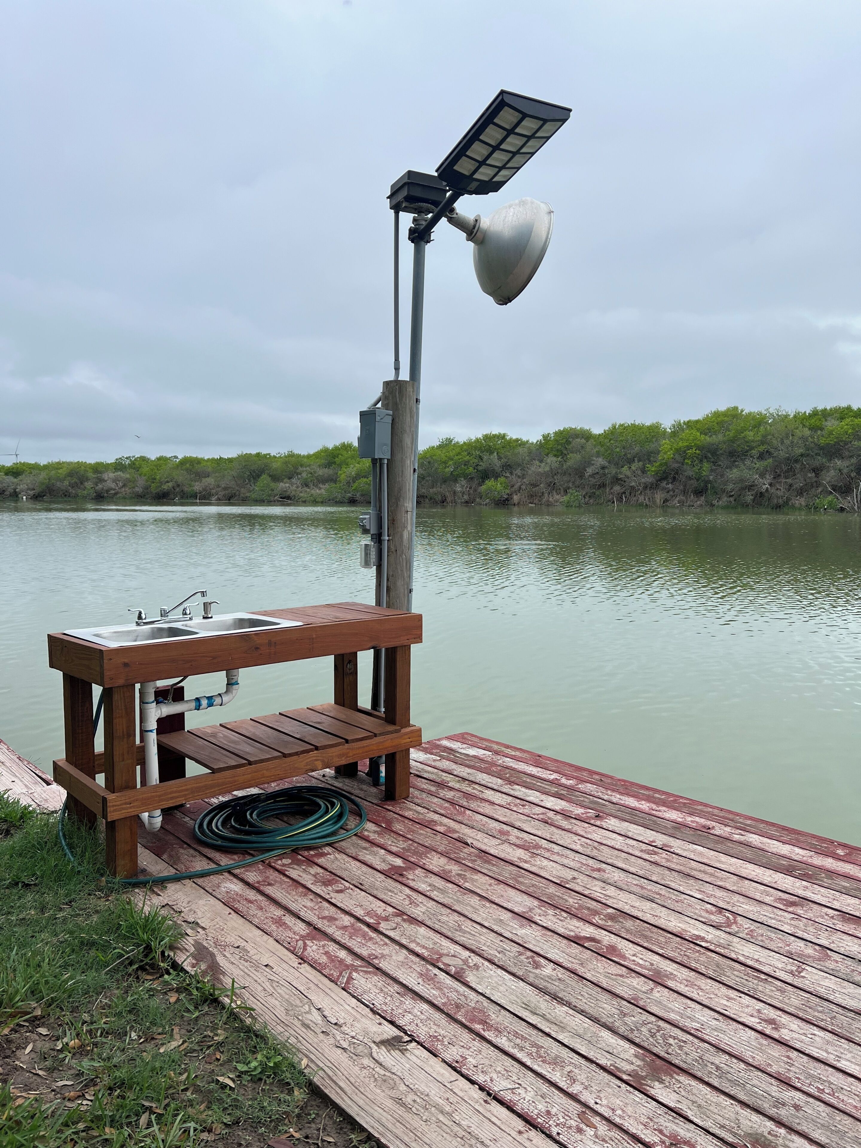 Un muelle de madera con un banco, un lavamanos y una lámpara con energía solar.