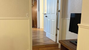 A hallway with wooden flooring, white walls, and a door leading to another room.