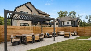 A patio area with outdoor furniture, a pergola, and a wooden fence. - Spacious New-Construction Home in Charming Bentonville! Prime location! (Bentonville)