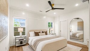 A bedroom with a bed, bedside tables, a ceiling fan, and a large window. - Spacious New-Construction Home in Charming Bentonville! Prime location! (Bentonville)