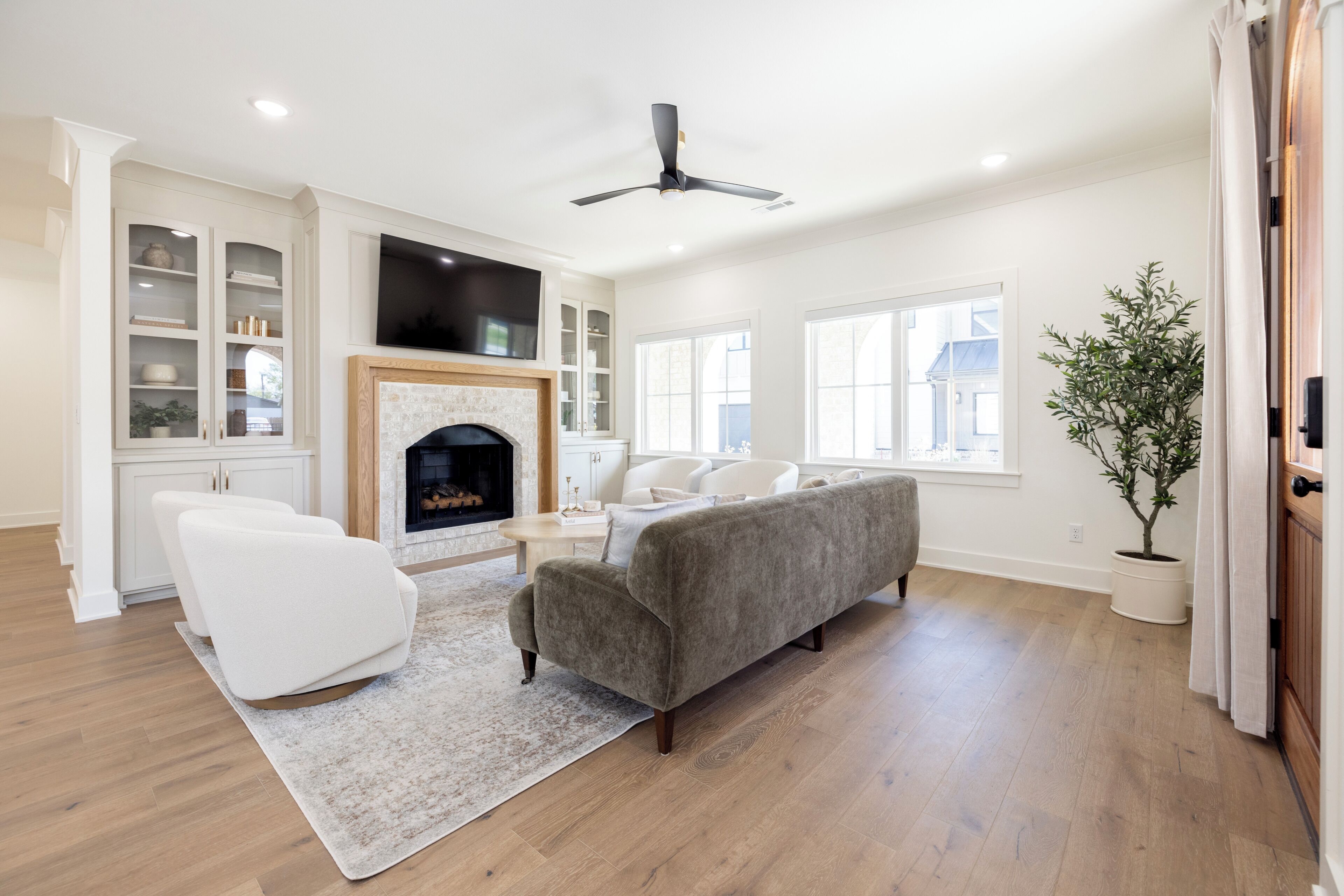 Un salón espacioso con chimenea, muebles blancos y un ventilador de techo.