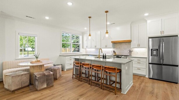 A modern kitchen with white cabinets, a stainless steel refrigerator, and a central island with stools. - Spacious New-Construction Home in Charming Bentonville! Prime location! (Bentonville)
