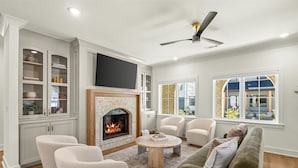 A living room with a fireplace, white furniture, and large windows. - Spacious New-Construction Home in Charming Bentonville! Prime location! (Bentonville)