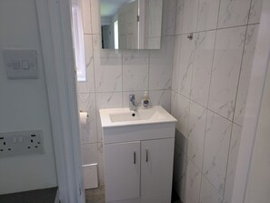 A bathroom with a white sink, mirror, and marble tiles. There is a door leading to another room. - Peaceful and Comfortable Guest Residence in Chorlton, Manchester (Manchester)