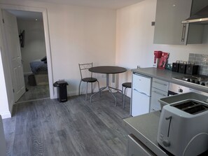 A compact kitchen with a dining table, chairs, a trash bin, a small refrigerator, and a toaster. - Peaceful and Comfortable Guest Residence in Chorlton, Manchester (Manchester)