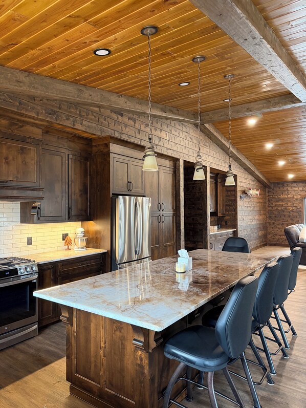 A modern kitchen with wooden cabinetry, a marble island, and bar stools.