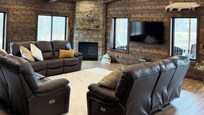 Una sala de estar acogedora con chimenea de piedra, sofás de cuero y televisor montado.