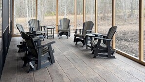 Un espacio de estar al aire libre con techo, sillas Adirondack y mesas, ventanas amplias y techo de madera.