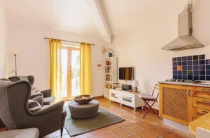 Ein Wohnzimmer mit einer Couch, einem Couchtisch, einem Fernseher und einer Küchenzeile mit Herd und Schränken.