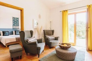 Ein Zimmer mit einem Bett, zwei Sesseln, einem kleinen Tisch und Blick durch eine Glastür.