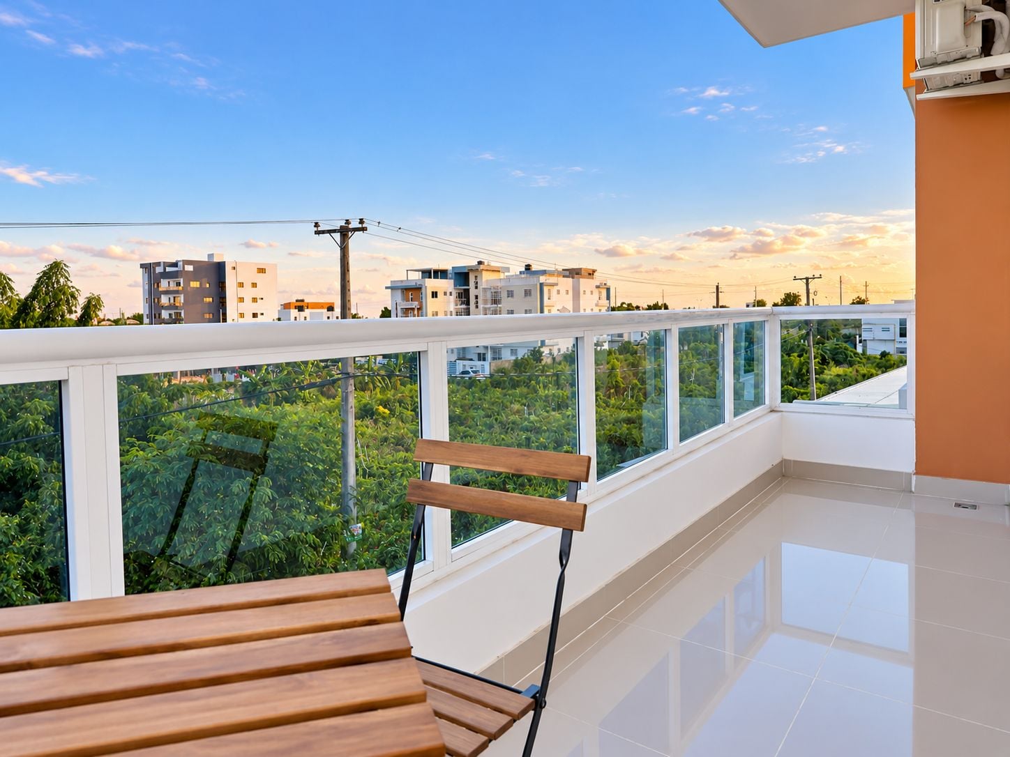 Ein Balkon mit einer Holzbank, Glasgeländer und Blick auf Gebäude und Grünflächen.