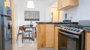 A modern kitchen with a built-in oven, a dining area with wooden chairs, and a pendant light.