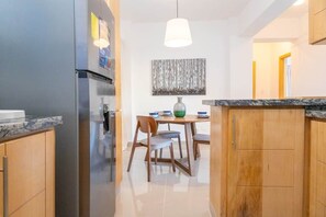 Une cuisine moderne équipée d’un réfrigérateur, de meubles de rangement en bois, d’une table à manger avec des chaises et d’un luminaire suspendu.