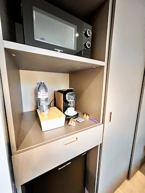 Eine Minibar mit einer Mikrowelle, einer Kaffeemaschine, einer Flasche Evian-Wasser, einer Tasse und Snacks.