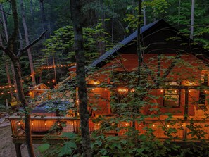 A cabin with a wooden exterior, surrounded by trees, and illuminated by string lights.