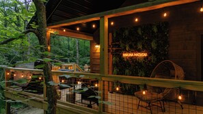 A wooden cabin with a balcony, a neon sign, and a wall with greenery.