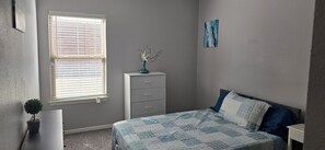 A bedroom with a bed, a dresser, a window with blinds, a small potted plant, and a painting on the wall. - Comfortable 3BR Home , Eastside El Paso, Family Friendly (El Paso)