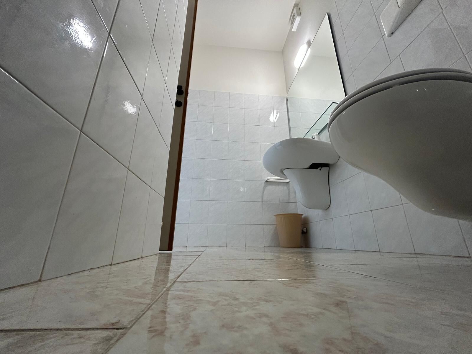 Un bagno con pareti piastrellate di bianco, un water e un cestino.