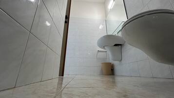 Un bagno con pareti piastrellate di bianco, un water e un cestino.