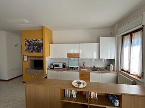 A compact kitchen with white cabinets, a microwave, a stove, and a sink. There's a wooden counter with a decorative plate and books. - Apartment ample parking and view of Assisi near the Porziuncola - Sole (Santa Maria degli Angeli)