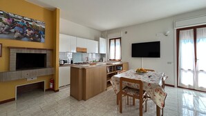 Ein Wohnzimmer mit Kamin, einem Essbereich mit Tisch und Stühlen, einer Küche mit Schränken und einem Fernseher, sowie eine gelbe Wand mit einem Familienfoto.