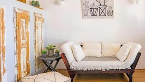 Un salon avec un canapé blanc, une petite table ronde ornée de plantes et une œuvre d’art représentant des cactus, accrochée au mur.