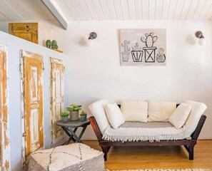 Ein Wohnzimmer mit einem weißen Sofa, einem kleinen runden Tisch mit Pflanzen und einem Wandbild mit Kakteen.