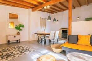 Ein Zimmer mit Holzboden, einem Esstisch mit Stühlen, einer Couch mit Kissen, einem kleinen Tisch mit Korb und einer Pflanze.