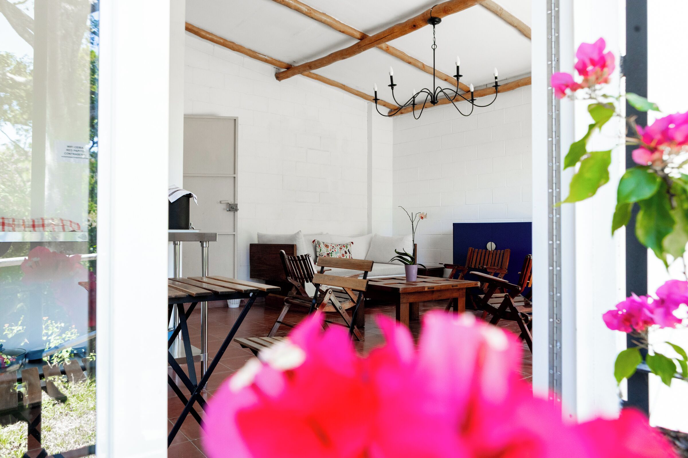 A room with a wooden ceiling, a chandelier, a white brick wall, and a table with chairs.
