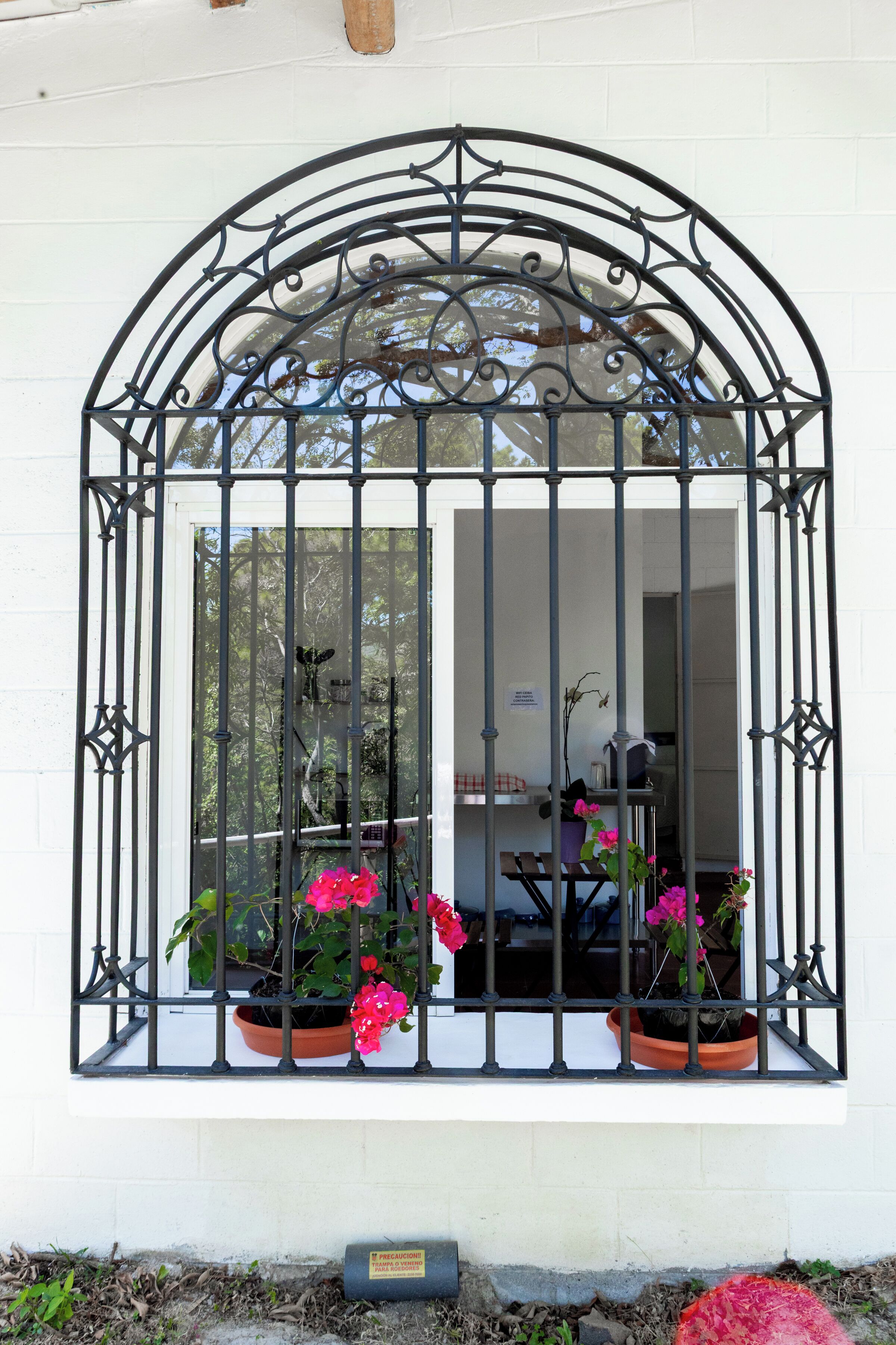 Una ventana con reja de hierro forjado, plantas en macetas y una pequeña mesa.