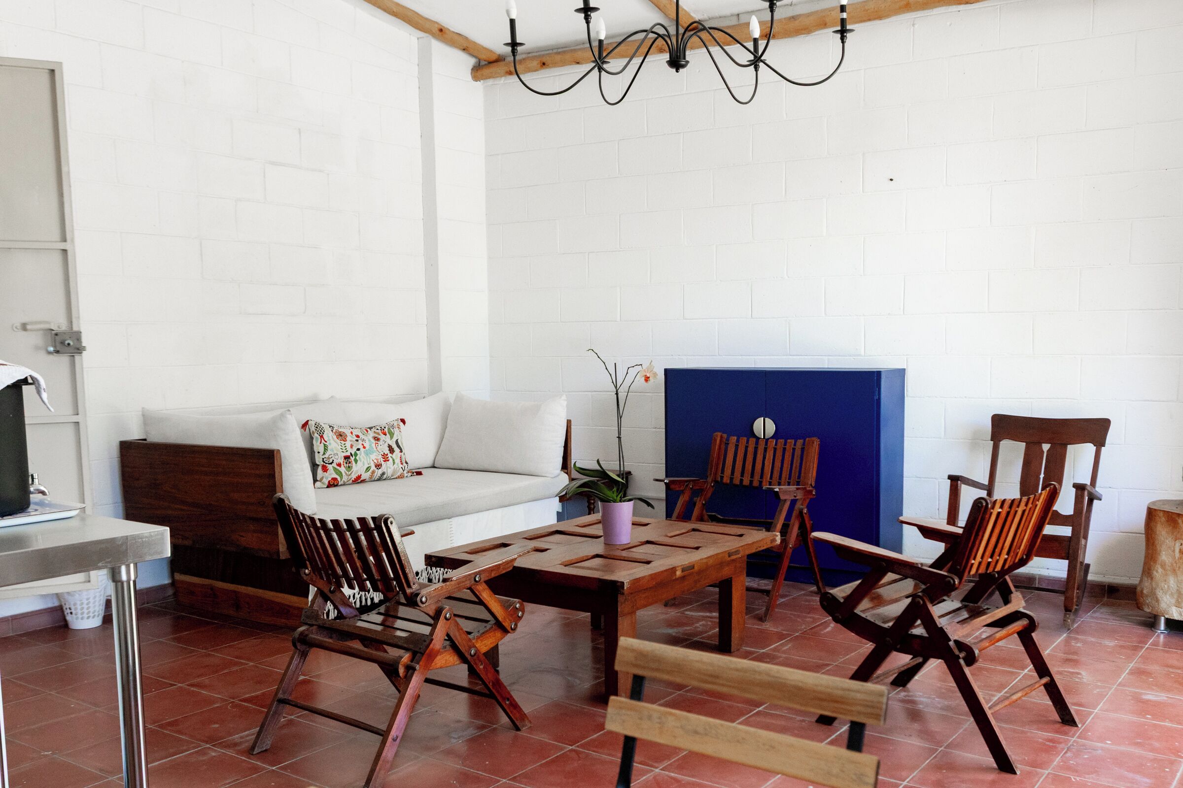Une pièce avec un mur en briques blanches, un plafond en bois, un canapé blanc, une table basse en bois et plusieurs chaises en bois.