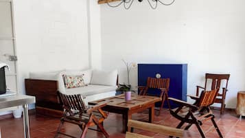 Une pièce avec un mur en briques blanches, un plafond en bois, un canapé blanc, une table basse en bois et plusieurs chaises en bois.