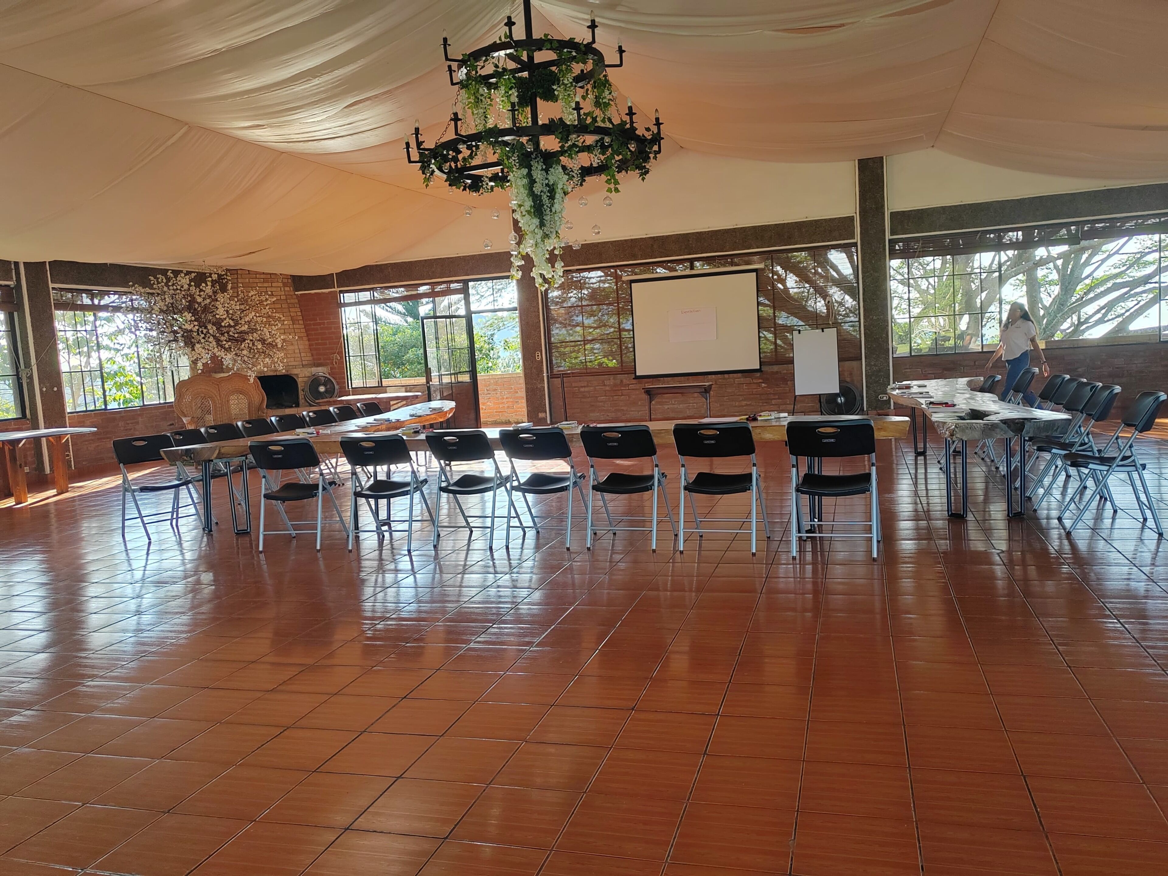 A conference room with a long table, chairs, a projector screen, and a chandelier.