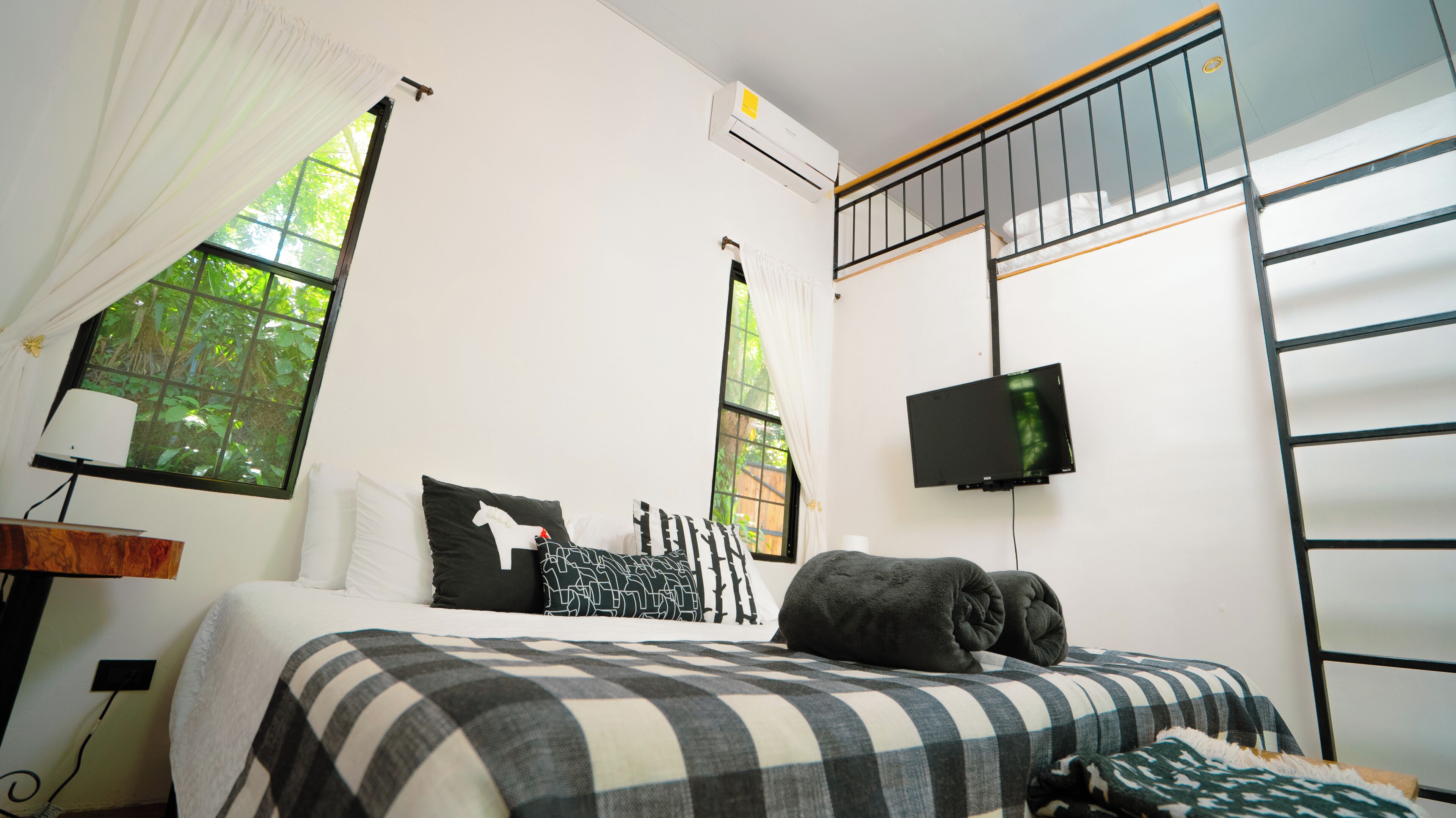 Un dormitorio con cama, televisión, ventana y ventilador de techo.