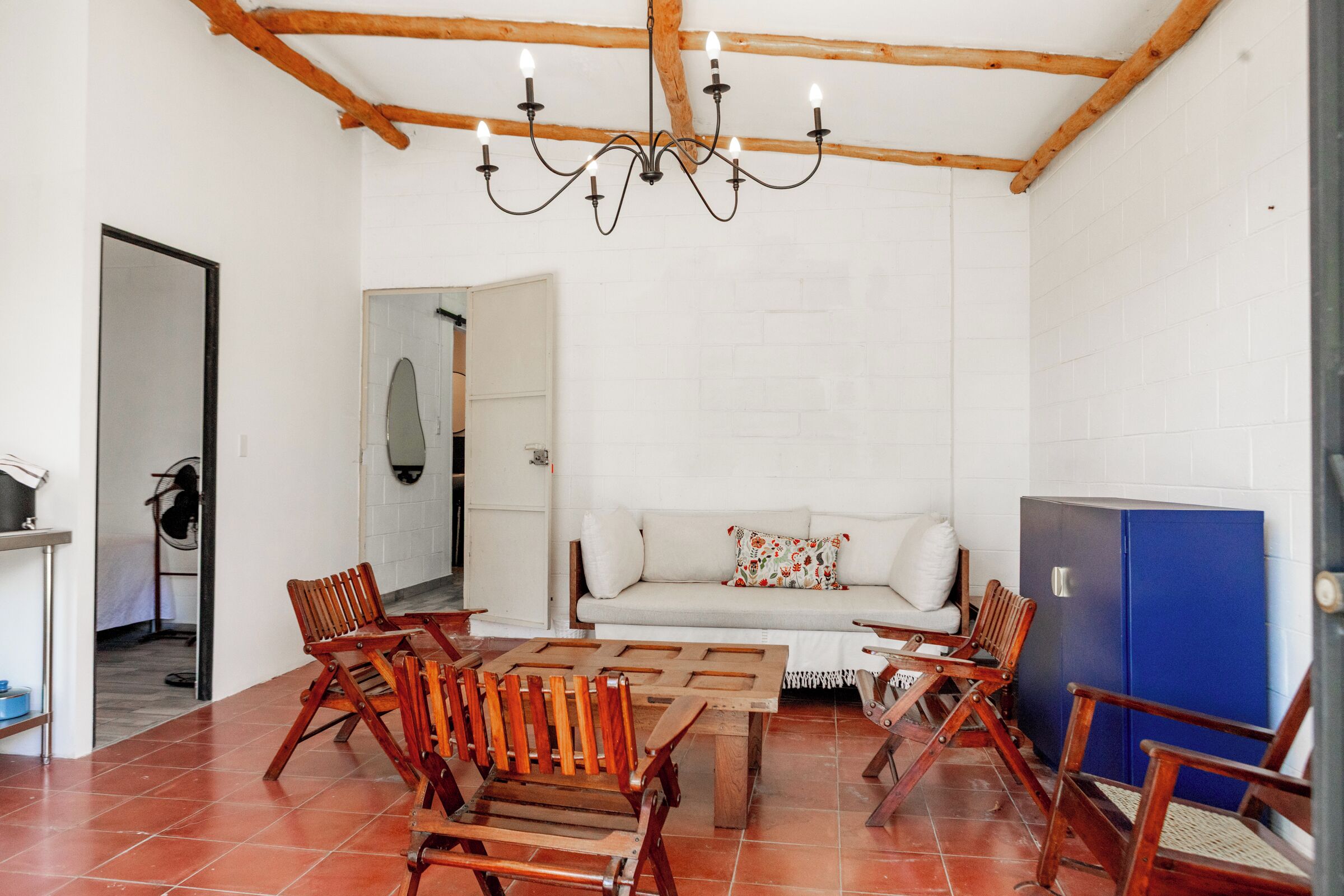 A room with a wooden ceiling, a chandelier, a sofa, and wooden chairs.