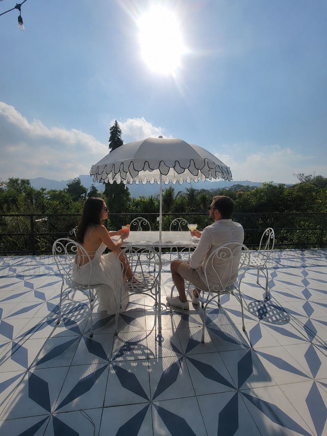 Two people seated at a table under a white umbrella on a tiled patio with a mountain view.