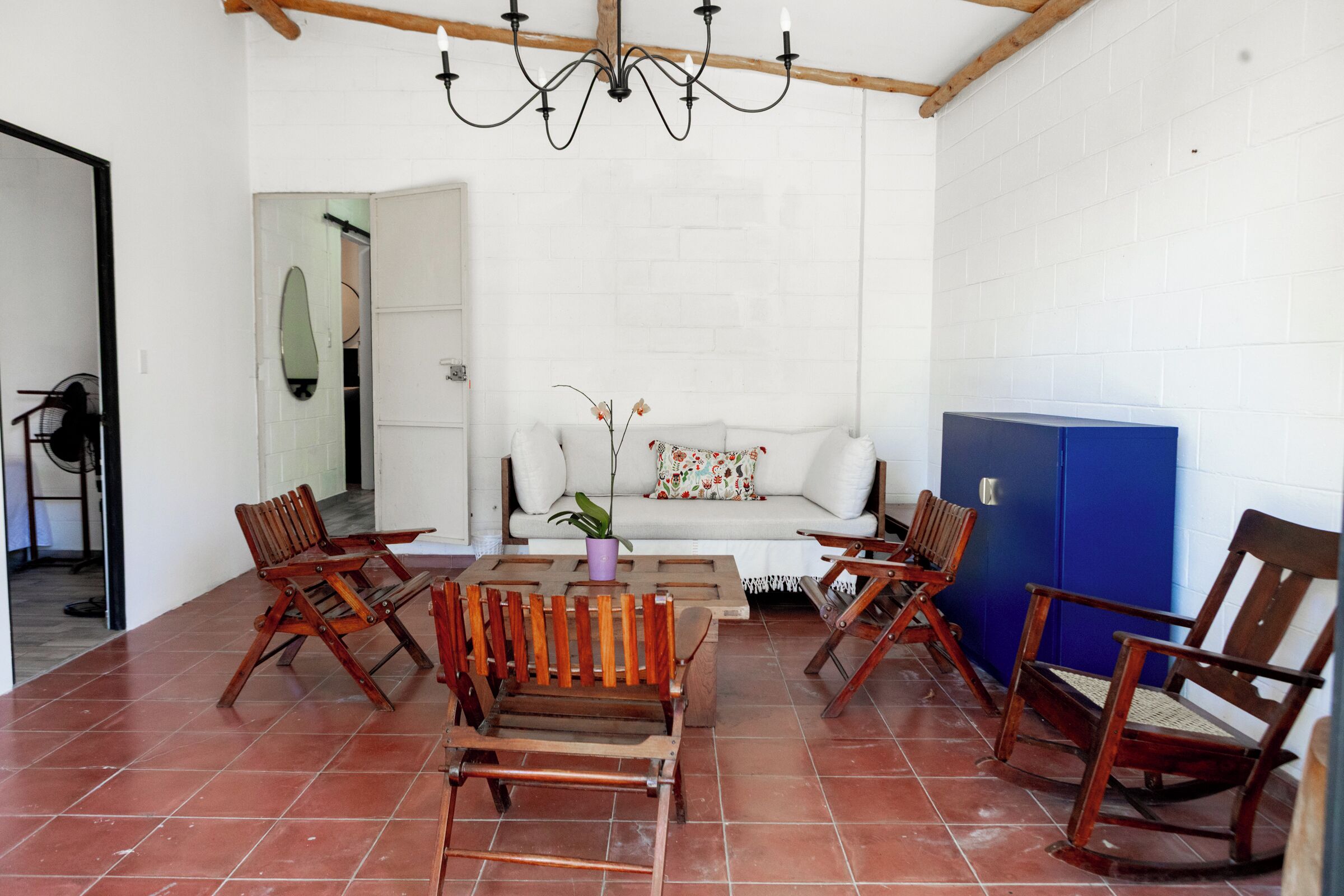 Una habitació amb una paret de maó blanc, un sostre de fusta, un sofà blanc, una taula de cafè i quatre cadires de fusta.