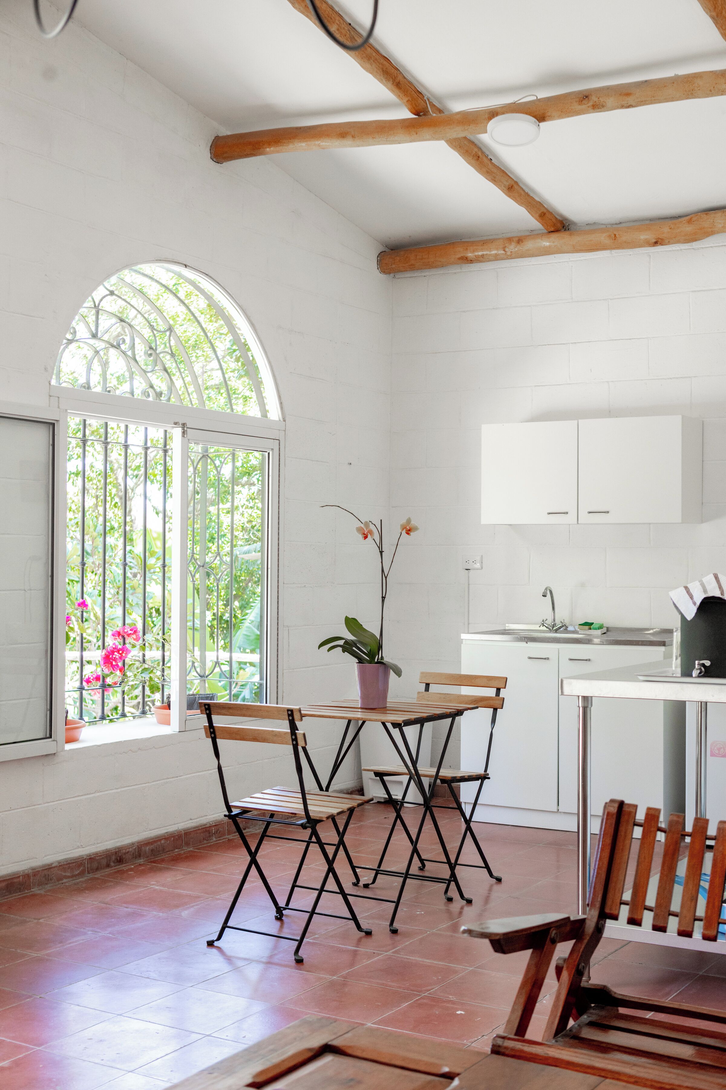 A kitchen with white cabinets, a wooden bench, and a window with a view of greenery.