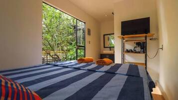 A room with a bed, a TV, a shelf with items, and a view of greenery.