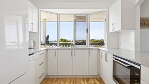 A modern kitchen with white cabinets, a built-in oven, and a large window overlooking a balcony. - Falcon Bayview Beach House - Large Pet-Friendly Falcon Bayview Beach House with Ocean Views (Falcon)