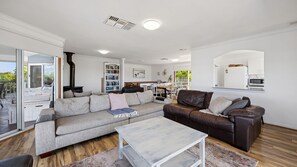 A modern living room with a sectional sofa, a coffee table, and a dining area with a kitchen in the background. - Falcon Bayview Beach House - Large Pet-Friendly Falcon Bayview Beach House with Ocean Views (Falcon)
